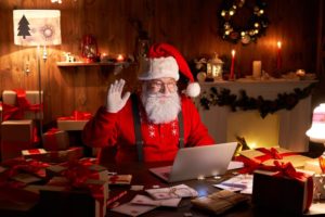 Santa sitting at his desk waiving to computer camera